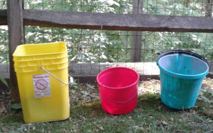 Image of three colored buckets sitting in front of a split rail fence
