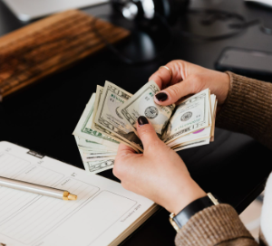 Hands holding a wad of money bills with a notebook and pen visible