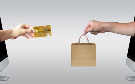 Image of two computer screens facing each other with a hand coming out of one holding a credit card and a hand coming out of the other holding a paper shopping bag courtesy Mediamodifier on Pixabay
