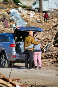 Photo of couple arm-in-arm while looking at a scene of destruction of homes