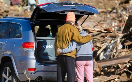 Photo of couple arm-in-arm while looking at a scene of destruction of homes