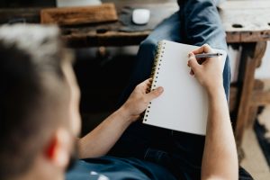 Image over the shoulder of a man starting to write on an empty pad of paper on his lap courtesy Peter Olexa on Unsplash