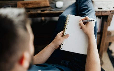 Image over the shoulder of a man starting to write on an empty pad of paper on his lap courtesy Peter Olexa on Unsplash