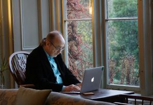 Photo of an older man sitting at a table by a window typing on a laptop courtesy Beth Macdonald on Unsplash