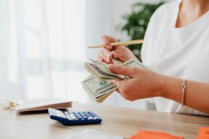 Photo of woman counting cash bills with calculator courtesy Kaboompics via Pexels