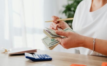 Photo of woman counting cash bills with calculator courtesy Kaboompics via Pexels