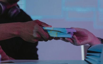Image of one hand handing a stack of money bills to another hand courtesy Pixels