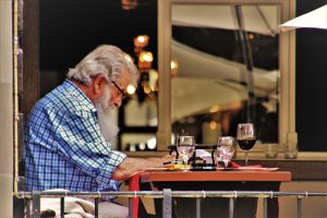 Image of an older man reading at an outdoor café table by Julita/Pixabay
