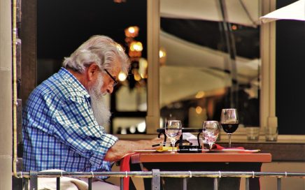 Image of an older man reading at an outdoor café table by Julita/Pixabay