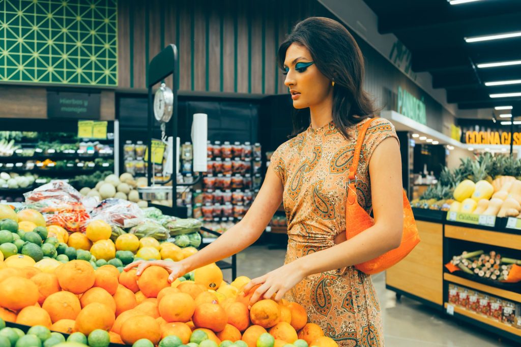 Photo of a high-fashion model looking over fruit in a grocery store courtesy of Rulo Davila - Pexels